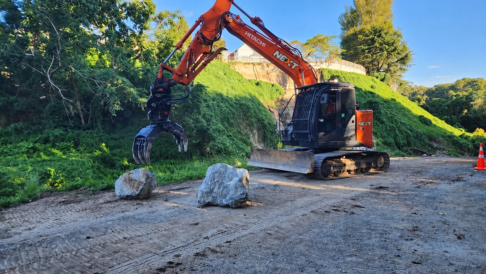 NEXT-branded excavator handling rock beside a hillside